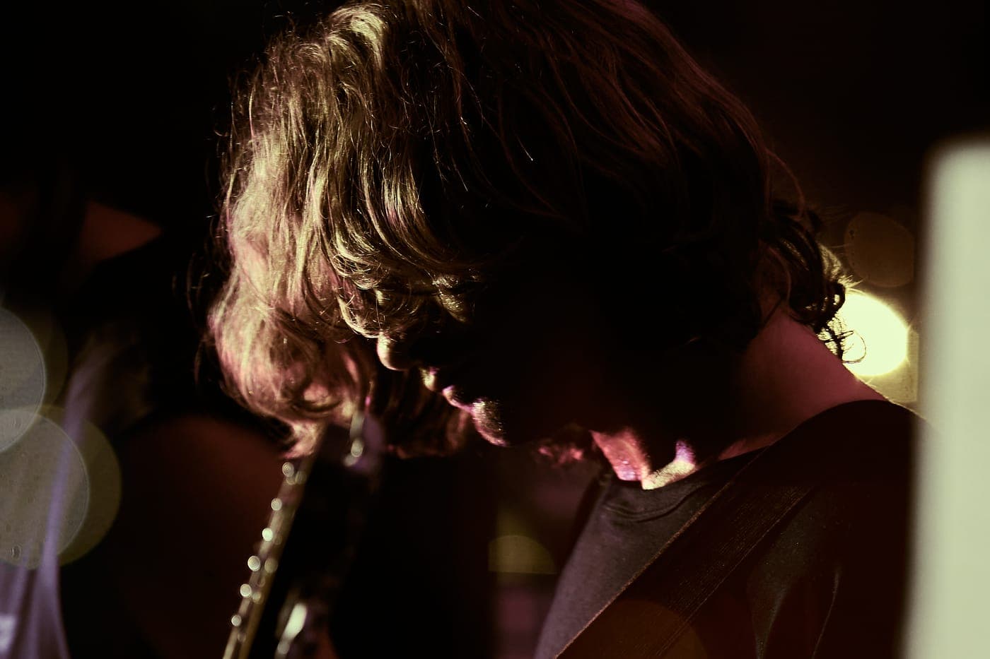 Close on the guitar, lit warm against the club lights